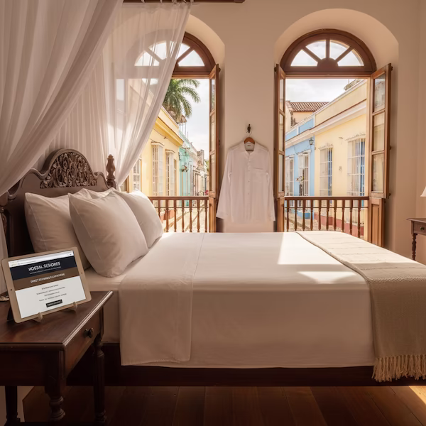 Habitación de lujo en un hostal colonial de Trinidad, Cuba, con una tablet que muestra el sistema de reservas directas.
